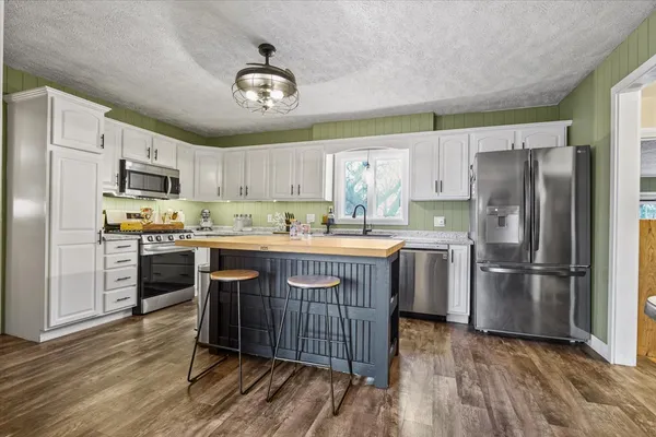 a kitchen with stainless steel appliances kitchen island granite countertop a refrigerator a stove a sink dishwasher and a dining table with wooden floor