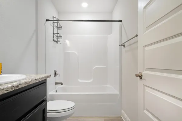 a bathroom with a granite countertop bathtub shower sink vanity and toilet
