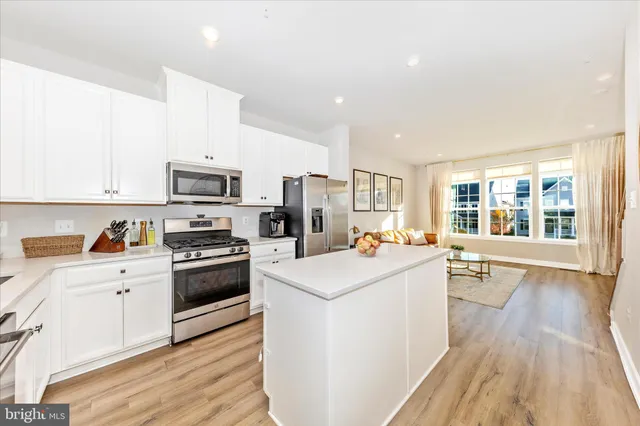 a kitchen with stainless steel appliances kitchen island granite countertop a stove a sink a refrigerator and a dining table with wooden floor