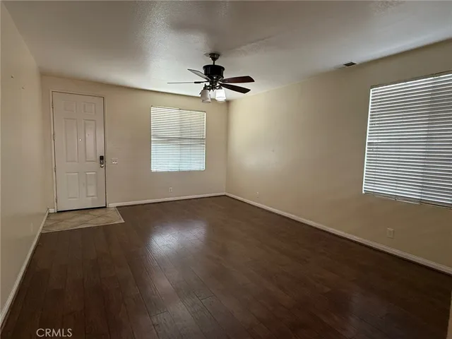 an empty room with wooden floor chandelier fan and windows