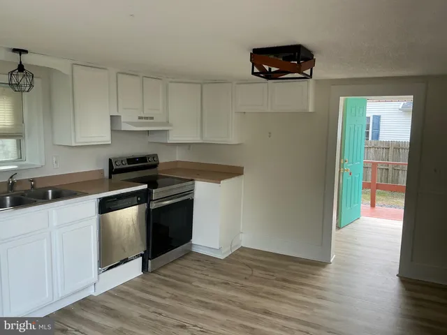 a kitchen with stainless steel appliances a sink dishwasher a stove and white cabinets with wooden floor