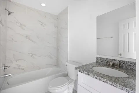 a bathroom with a granite countertop sink a toilet a mirror a bathtub and shower