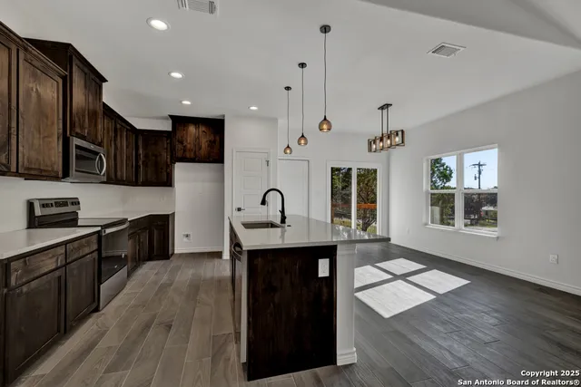 a kitchen with stainless steel appliances kitchen island granite countertop a stove a sink a refrigerator and cabinets with wooden floor