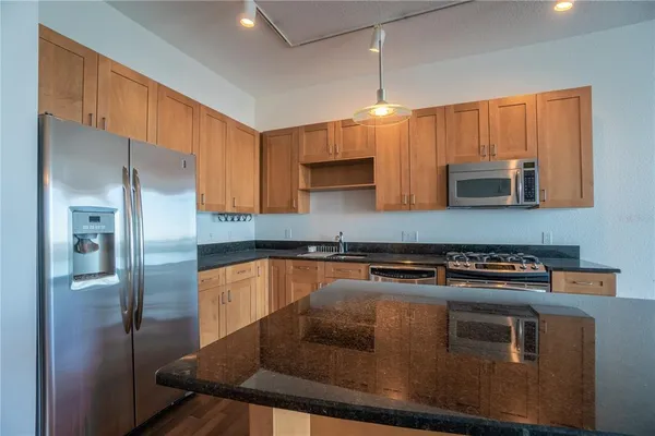 a kitchen with stainless steel appliances granite countertop a refrigerator a stove and a sink with wooden floor