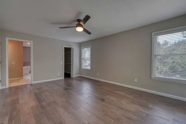 a view of an empty room with wooden floor and a ceiling fan