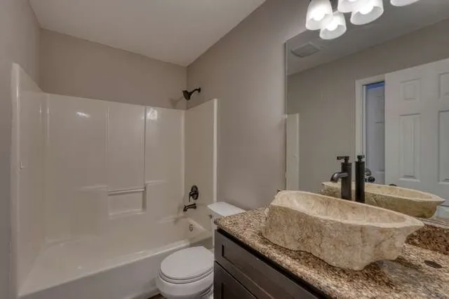 a bathroom with a granite countertop sink a toilet a mirror and shower