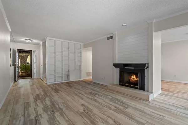 a view of an empty room with wooden floor fire place and a window
