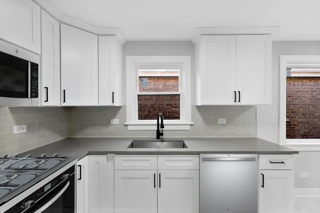 a kitchen with granite countertop a sink stainless steel appliances white cabinets and a window