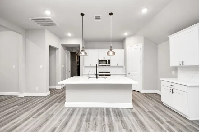 a large white kitchen with a stove a sink dishwasher and a refrigerator with wooden floor
