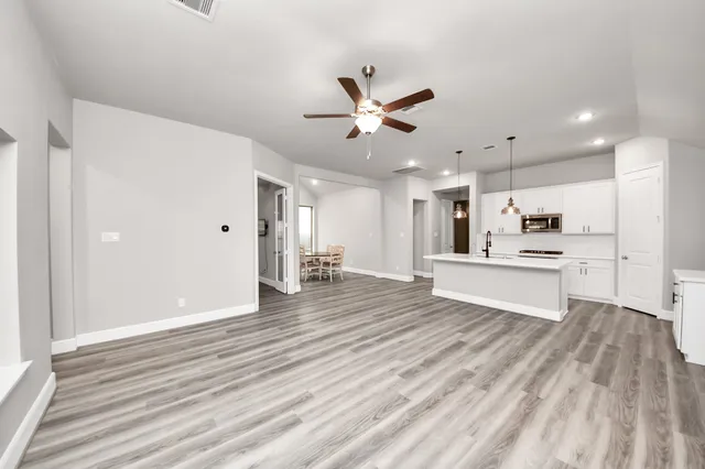 a view of an empty room with window wooden floor and a kitchen view