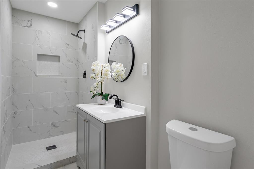 4815 Kelman Street Dallas, TX 75214 - Photo 24 of 37 Bathroom featuring a gray vanity with a white countertop, a black circular mirror, and a three-light vanity fixture