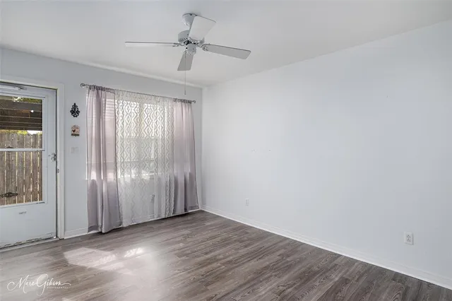 an empty room with wooden floor chandelier fan and windows