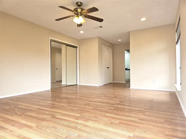 a view of an empty room with wooden floor and a ceiling fan