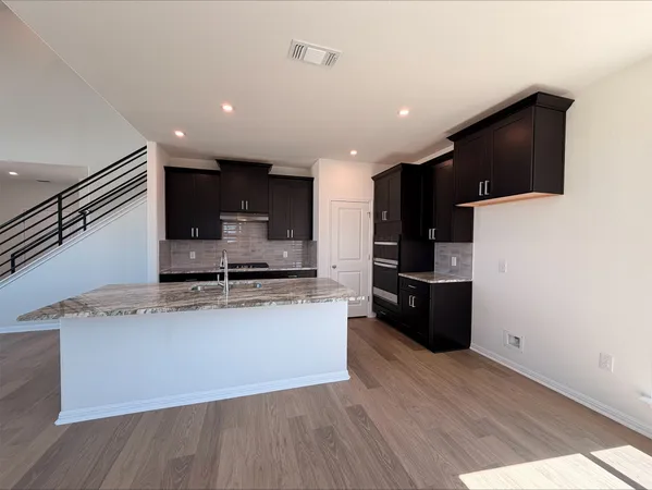 a large kitchen with stainless steel appliances kitchen island granite countertop a stove a refrigerator and a sink with wooden floor