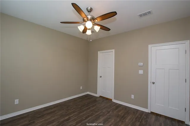 an empty room with wooden floor fan and windows