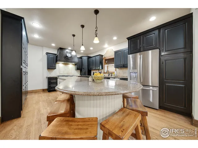 a kitchen with stainless steel appliances granite countertop a refrigerator a sink dishwasher a stove and a dining table with wooden floor