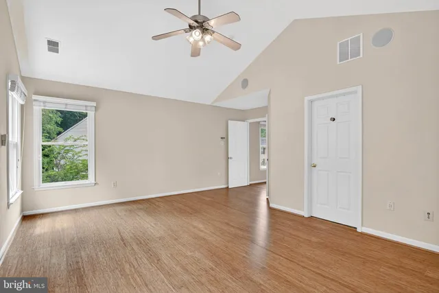 an empty room with wooden floor chandelier fan and windows