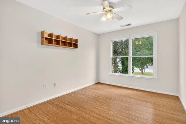 an empty room with wooden floor chandelier fan and windows