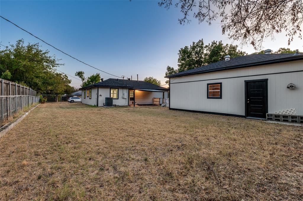 514 Chickapoo Trace Grand Prairie, TX 75051 - Photo 23 of 25 Expansive backyard featuring a privacy fence, an auxiliary building with a dark-paneled door, and a covered patio area