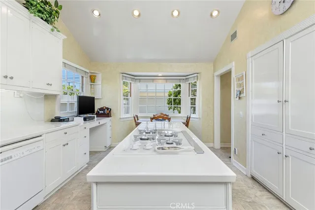a large white kitchen with kitchen island a stove a refrigerator a sink dishwasher and white cabinets with wooden floor