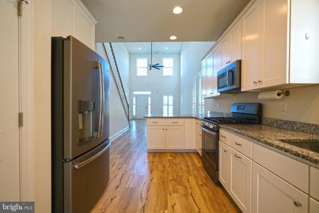 a large kitchen with stainless steel appliances granite countertop a refrigerator a oven and white cabinets with wooden floors