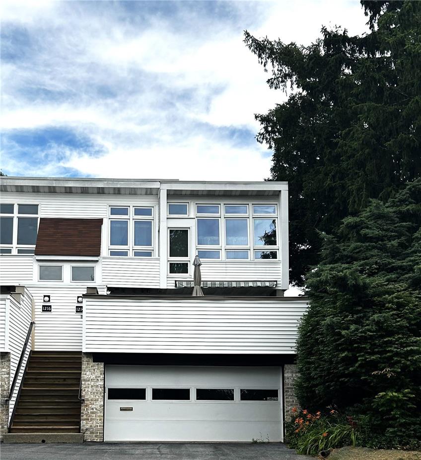 Modern facade with a spacious garage and inviting entry stairs, framed by mature evergreens.