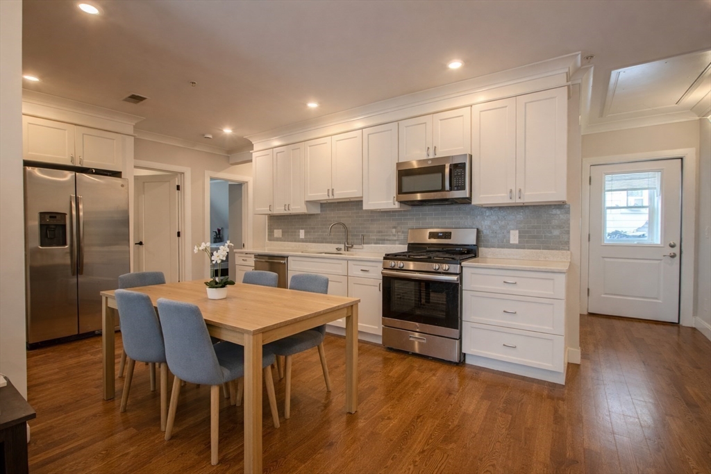 53 Quint Avenue, Unit 3 Boston, MA 02134 - Photo 12 of 18 a kitchen with stainless steel appliances a stove top oven a refrigerator a sink and a dining table with wooden floor