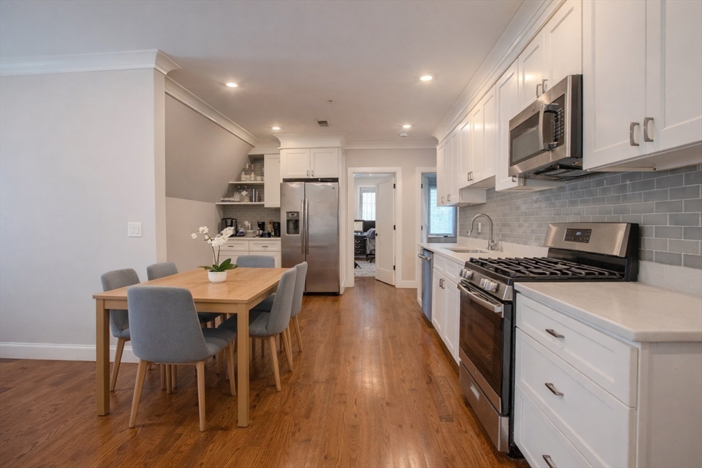 53 Quint Avenue, Unit 3 Boston, MA 02134 - Photo 6 of 18 a large kitchen with stainless steel appliances kitchen island granite countertop a stove a refrigerator a microwave a dining table and chairs with wooden floor