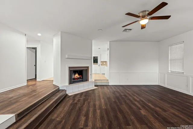 a view of a livingroom with a fireplace a ceiling fan and wooden floor