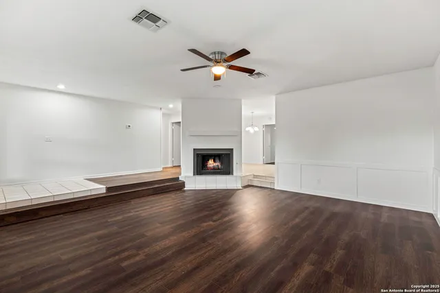 an empty room with wooden floor a ceiling fan a fireplace and windows