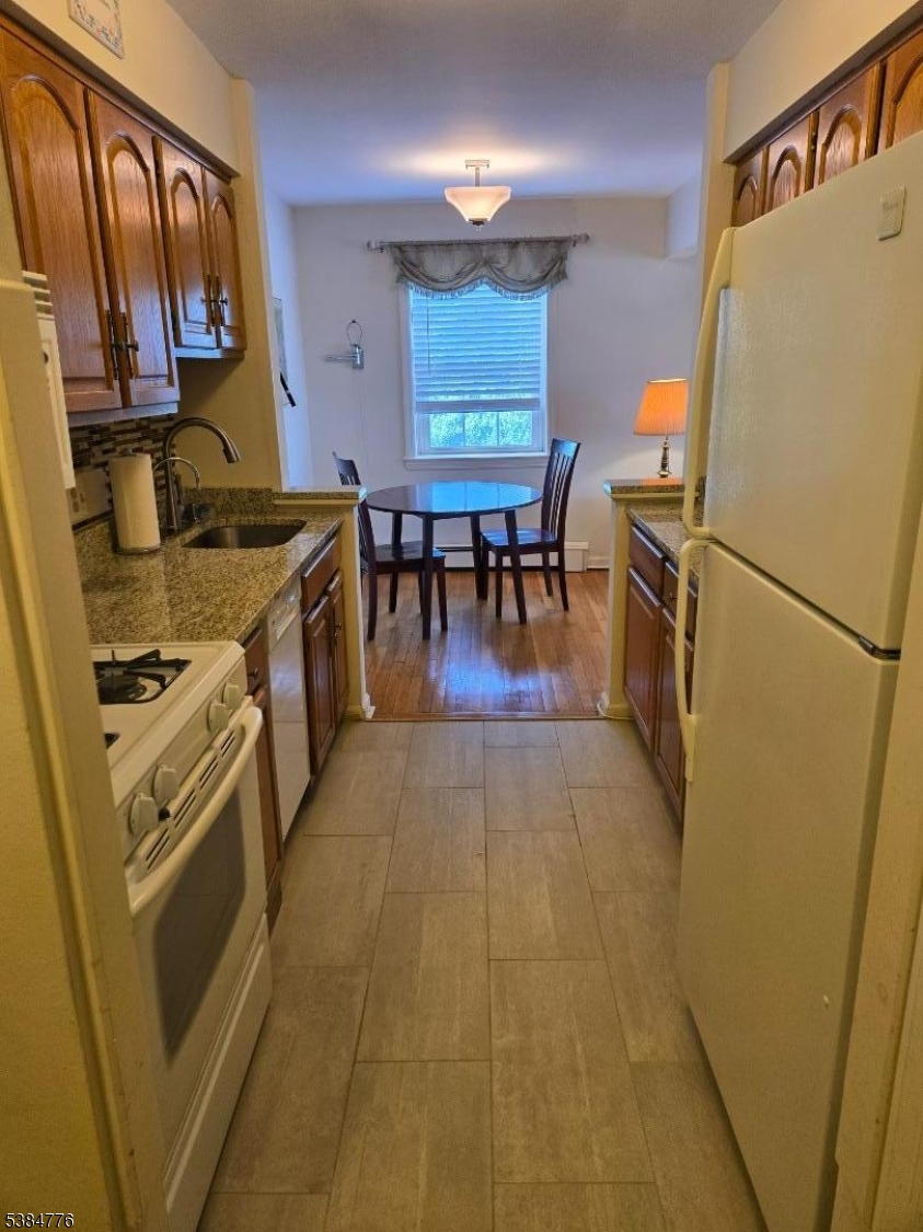 565 Grove Street, Unit C15 Clifton, NJ 07013 - Photo 3 of 11 a kitchen with stainless steel appliances a refrigerator a stove a sink a dining table and chairs with wooden floor