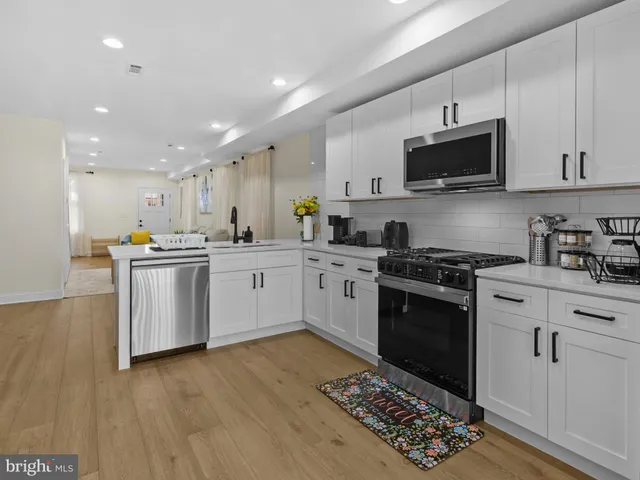 a kitchen with stainless steel appliances white cabinets a sink a stove a microwave and wooden floors