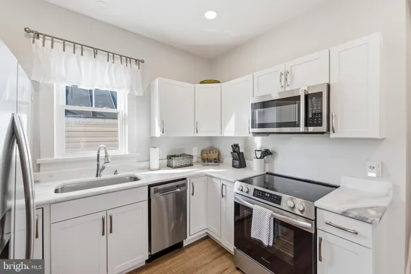 a kitchen with stainless steel appliances granite countertop white cabinets a sink a stove a microwave and wooden floors