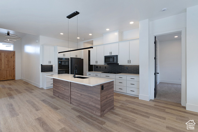 3145 Snow Cyn Road Hurricane, UT 84737 - Photo 6 of 38 Kitchen featuring light wood-style flooring, tasteful backsplash, light countertops, a kitchen island with sink, and black appliances