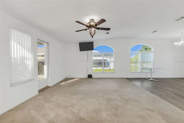 a view of an empty room with window and chandelier fan