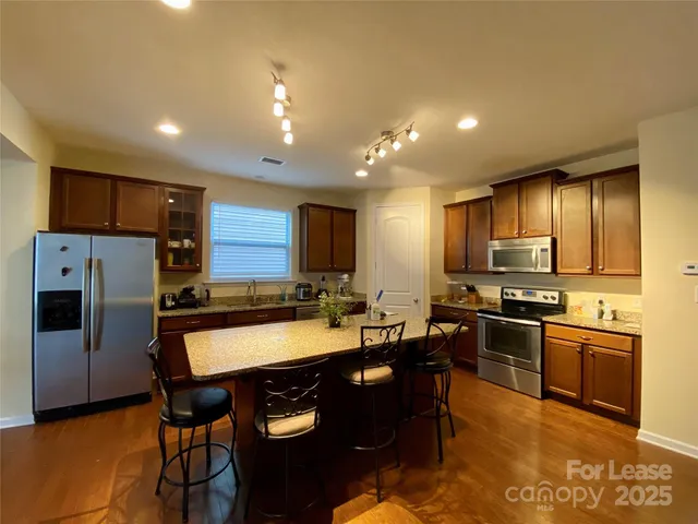 a kitchen with stainless steel appliances granite countertop a refrigerator a stove a sink a dining table and chairs
