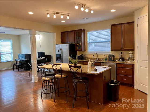 a kitchen with stainless steel appliances granite countertop a refrigerator a sink dishwasher a stove and a dining table with wooden floor