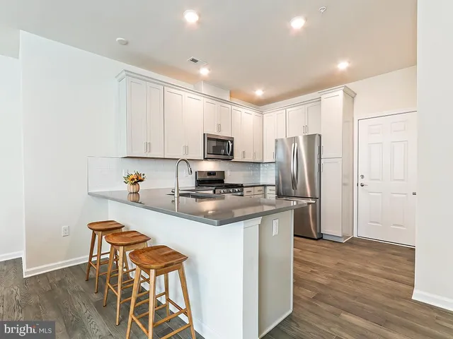 a kitchen with stainless steel appliances granite countertop a stove a sink a refrigerator and white cabinets with wooden floor