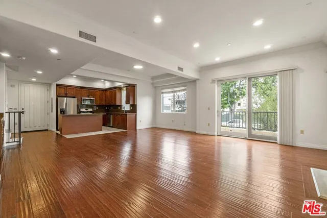 a view of an empty room with wooden floor and a kitchen