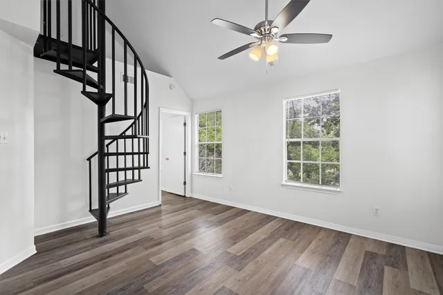 an empty room with wooden floor fan and windows