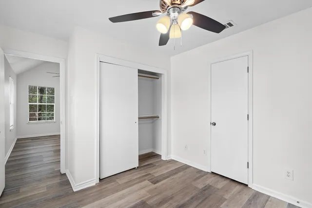 an empty room with wooden floor chandelier fan and windows