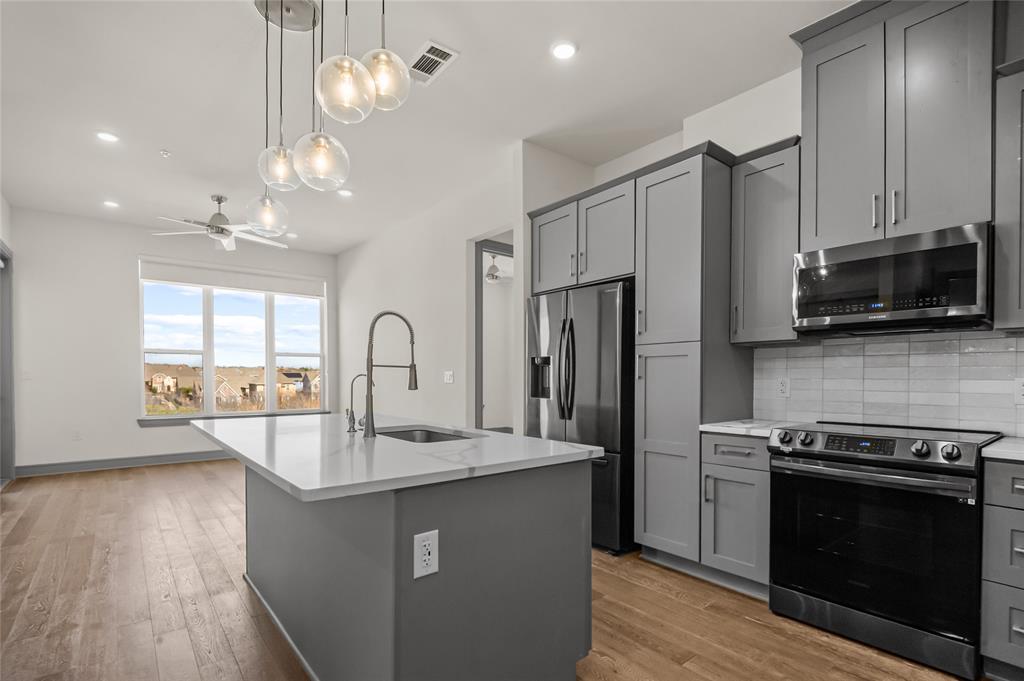 Kitchen featuring stainless steel appliances, gray cabinetry, a ceiling fan, and light stone countertops