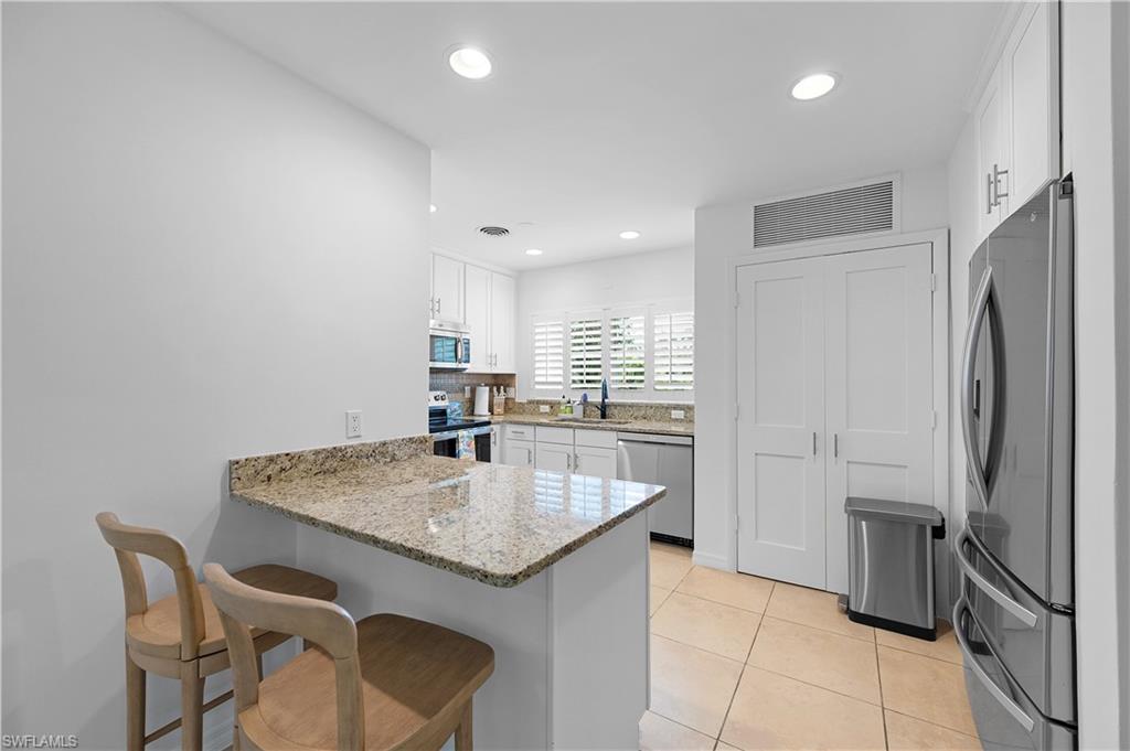 1340 Crayton Road, Unit 4 Naples, FL 34102 - Photo 10 of 22 Kitchen featuring light stone counters, a peninsula, a kitchen bar, stainless steel appliances, and white cabinets