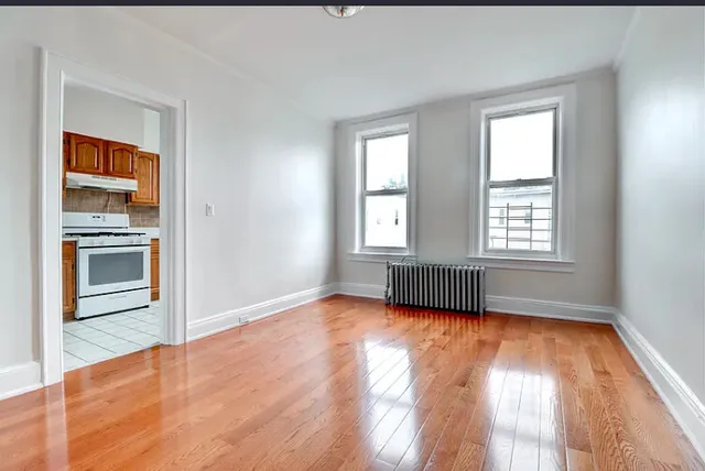 an empty room with wooden floor cabinet and windows