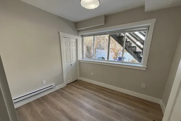 a view of an empty room with wooden floor and a window