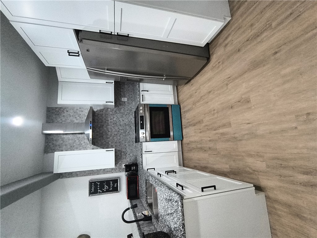 a kitchen with stainless steel appliances granite countertop a refrigerator a stove a sink and white cabinets with wooden floor