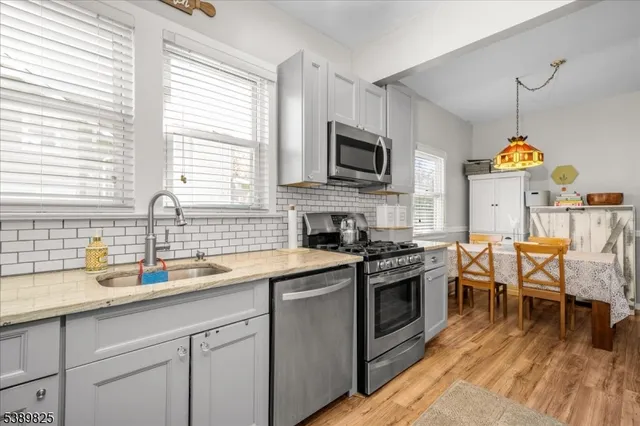 a kitchen with stainless steel appliances granite countertop a sink a stove top oven a chimney cabinets and living room view