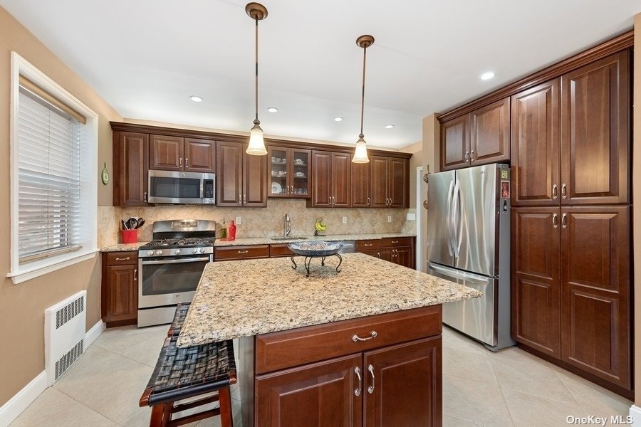 a kitchen with kitchen island granite countertop a refrigerator a sink a stove a oven and chairs