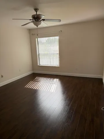 an empty room with wooden floor chandelier fan and windows