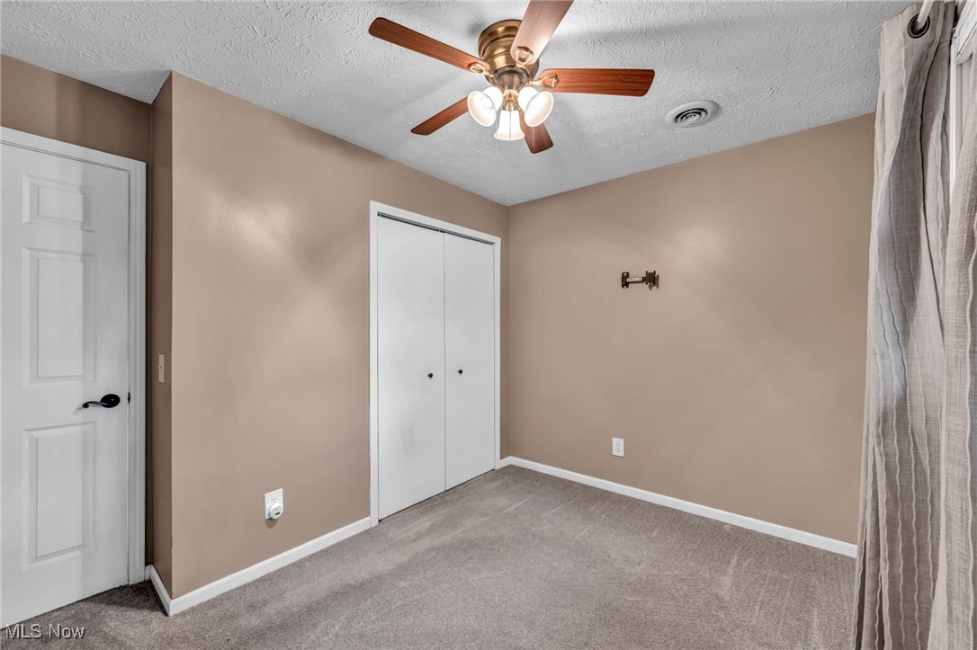 47655 Cooper Foster Park Road Amherst, OH 44001 - Photo 16 of 49 Unfurnished bedroom featuring carpet, a textured ceiling, a closet, and a ceiling fan